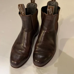 Bruna chelsea boots från Ian Harolds - Klassiska bruna chelsea boots från Ian Harolds i äkta skinn. Snygg rund tå, elastiska paneler på sidorna och dragflikar med logga för enkel påtagning. Perfekta för dig som gillar tidlös och stilren look.