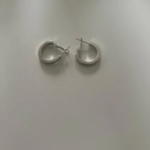 Silvriga hoops örhängen - Stilrena silvriga hoops med klassisk rund form. Perfekta för dig som gillar minimalistiska smycken med lite extra edge. Lätta att matcha med olika outfits och har ett smidigt lås som håller dem på plats hela dagen.