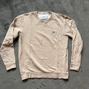 Beige sweatshirt från Les Deux - Snygg beige sweatshirt från Les Deux med rund halsringning och diskret logga på bröstet. Tröjan har långa ärmar och ribbade muddar vid ärmslut och nederkant. Perfekt för en chill och stilren look. Stl M