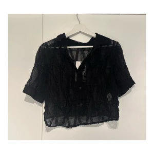Svart transparent skjorta / blus från Zara - Säljer en svart, transparent skjorta / blus från Zara med korta ärmar och krage. Skjortan har cropped stil och knappar framtill. Aldrig använd, lappen kvar.