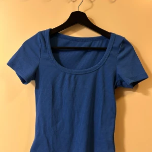 Blå ribbad topp med rund hals - En enkel och stilren blå ribbad topp med korta ärmar och rund, djup ringning. Perfekt att matcha med jeans eller kjol för en avslappnad look. Toppens material är stretchigt och sitter snyggt mot kroppen.