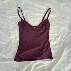 Vinröd linnetopp från Zara - Säljer en vinröd linnetopp från Zara med smala axelband och v-ringad skärning. Toppen är figurnära och har en enkel, stilren design som passar perfekt till jeans eller kjol. Materialet är mjukt och bekvämt, perfekt för varma dagar.