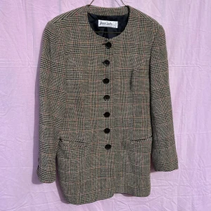 Rutig kavaj från Jean Claire, stl 38 - Snygg rutig kavaj från Jean Claire i grått, svart och röda detaljer. Klassisk rak modell med rund halsringning, stora svarta knappar framtill och fickor. Tillverkad i ullblandning för en stilren och tidlös look. Perfekt för dig som gillar preppy vibes.