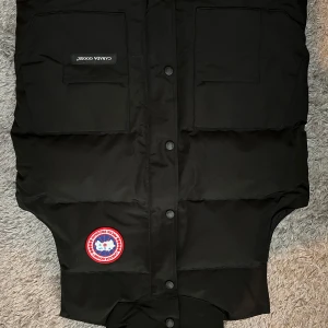 Helt ny väst - Svart väst. Västen har två stora fickor framtill, knäppning med knappar.