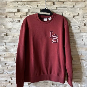 Mörkröd sweatshirt med LS-tryck - Säljer en mörkröd sweatshirt från Levis med LS-bokstäver broderade på bröstet. Tröjan har rund hals och långa ärmar. Perfekt för chill dagar eller när du vill ha en enkel och snygg look.