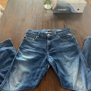 Helt nya! Replay Sandot blå tapered jeans 32 - (byte funkar också mot ett likanande mindre par) Säljer ett par Replay Sandot jeans i blå tvätt med snygga slitningar och kontrastsömmar. Modellen är relaxed tapered med klassiska fem fickor och logga på bakfickan. Perfekt passform för dig som gillar lite mer avslappnad stil men ändå vill ha smalare ben.