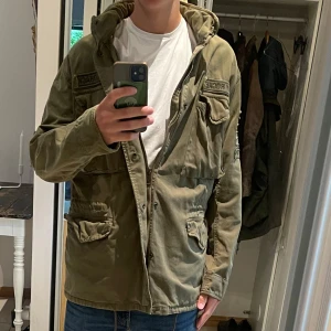 Grön höstjacka - PRIS ÄR DISKUTERBART. Säljer en grön parkajacka från Rock Creek med coola patchar och detaljer på ärmen. Militärjackam har flera fickor med lock, huva och dragkedja framtill. Field jacka är perfa för hösten och vintern
