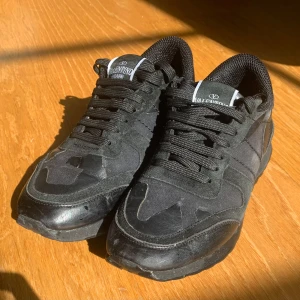 Svarta sneakers från Valentino Garavani - Snygga svarta sneakers från Valentino Garavani med klassisk design. Skorna har snörning, rund tå och är tillverkade i en mix av mocka, skinn och textil. Perfekta för dig som gillar stilrena och exklusiva sneakers med streetkänsla. Storlek är 37-38. Hör av er vid minsta fråga!🤩