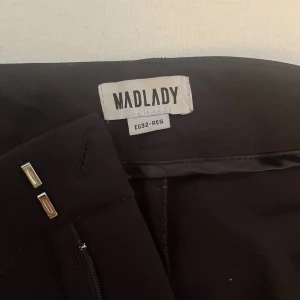 Svarta kostymbyxor från Madlady - Snygga svarta kostymbyxor från Madlady med låg midja och raka pressveck framtill. Säljes då de är förstora. Storlek 32/regular! Köpta för 650kr, säljes för 250!
