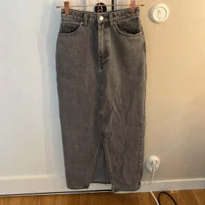 Grå lång jeanskjol från Monki - Säljer en grå lång jeanskjol från Monki i klassisk femficksmodell. Kjolen har en rak passform, slits framtill och snygga bakfickor. Perfekt för dig som gillar en chill och stilren look. Passar till sneakers eller boots.❤️