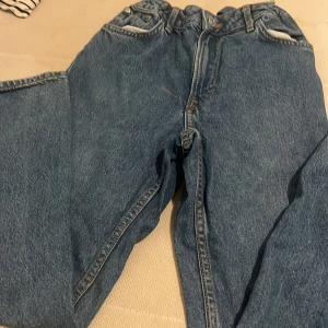 Blå baggy jeans med hög midja - Säljer ett par klassiska blå jeans med baggy passform och hög midja. Jeansen har stora bakfickor, bälteshällor och dragkedja framtill. Perfekta för en avslappnad och trendig look. Materialet är robust denim som håller länge.
