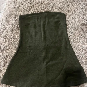 Olivgrön tubtopp från Gina Tricot - En stilren olivgrön tubtopp från Gina Tricot i mjukt stretchigt material. Toppen är axelbandslös och har en enkel, rak design som sitter tajt mot kroppen. Perfekt att matcha med jeans eller kjol för en clean look.