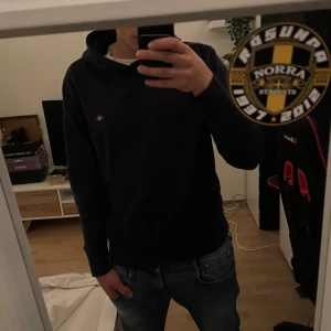 mörkblå hoodie från Gant - Säljer en mörkblå hoodie med broderad logga på bröstet. Klassisk modell med huva och långa ärmar, perfekt för en chill och avslappnad stil. Passar dig som gillar streetwear och enkel design.
