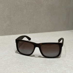 Ray-Ban Justin solglasögon brun - Snygga Ray-Ban Justin solglasögon i brunmelerad plast med fyrkantig form. Modellen har breda skalmar och mörka tonade glas. Perfekta för dig som vill ha en cool och tidlös look. Modellnummer RB4165.