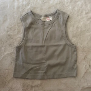 Grå ribbad linnetopp från H&M - Säljer en ljusgrå ribbad linnetopp från H&M. Toppen är ärmlös och croppad med rund halsringning och mjuk bomullskänsla. Perfekt till jeans eller kjol för en chill och enkel look.