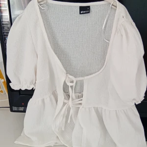 Vit blus med knyt från Gina Tricot - Superfin vit blus från Gina Tricot med puffiga korta ärmar och knyt framtill. Blusen har en luftig, strukturerad bomullskänsla och volangdetaljer nedtill. Perfekt för en fräsch och trendig look i sommar eller vår. har använt denna 1 gång sen jag köpte den i vintras på rean❤️Bra skick inga tecken på användning