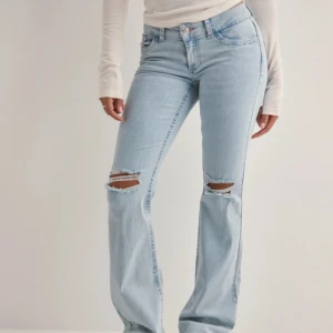 Ljusblå bootcut jeans med slitningar - Säljer ett par ljusblå jeans från Nelly med bootcut passform och snygga slitningar vid knäna. Jeansen har klassisk femficksdesign, rosa -söm på bakfickan och är tillverkade i mjukt jeansmaterial. Perfekt för dig som gillar en chill och trendig look