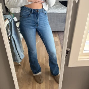 Bootcut jeans i ljusblå denim - Snygga ljusblå bootcut jeans med hög midja och klassisk femficksdesign. Jeansen har en smickrande passform som sitter tajt över låren och släpper ut vid bensluten. Tillverkade i mjuk och stretchig denim för extra komfort.