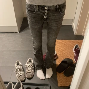 Grå bootcut jeans från H&M, stl 146 - Säljer ett par grå bootcut jeans från H&M i storlek 146. Jeansen har låg midja, justerbar midja och flera knappar framtill. Snygg tvättad grå färg och klassisk femficksmodell. Perfekta för dig som gillar en avslappnad men trendig look.
