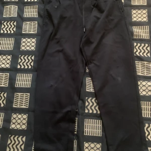 Svarta mjukisbyxor från H&M Regular Fit - Svarta mjukisbyxor från H&M i regular fit med elastisk midja och dragsko. Byxorna har raka ben och en bakficka, perfekta för en chill och avslappnad stil. Sköna och enkla att matcha med det mesta. Det har bara ett litet hål på högra knät