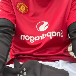 Manchester United Mainoo 37 matchtröja - Röd Manchester United fotbollströja med Mainoo 37 på ryggen och SnapDragon som sponsor framtill. Klassisk design med vita detaljer på axlarna och klubbmärke på bröstet. Tillverkad i lätt och ventilerande material, perfekt för fotbollsplanen.