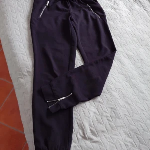 Svarta mjukisbyxor från Amisu, strl 34 - Svarta mjukisbyxor från Amisu med elastisk midja och snörning. Byxorna har två fickor med dragkedja framtill och muddar vid bensluten. Perfekta för chill eller häng med kompisar. Snygg och enkel design som funkar till det mesta.