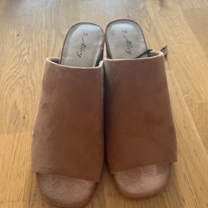 Beige sandaler från Alley, storlek 38 - Säljer ett par snygga sandaler från Alley i beige mocka. Modellen har öppen tå och platt sula, med en stilren och enkel design som passar perfekt till varma dagar. Materialet är mjukt och ger en skön känsla mot foten.