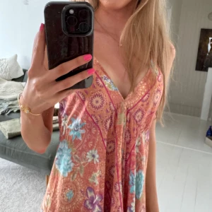 Blommig sommarklänning med volang - Säljer en luftig och färgglad klänning med blommigt mönster i orange, blått och rosa köpt utomlands! Klänningen har v-ringning, volang nertill och öppen rygg med snörning. Perfekt för varma dagar och har en avslappnad passform. Passar som strandklänning då den är väldigt luftig💓 Jag är 173 för referens! aldrig använd<3