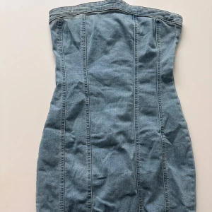 Jeansklänning från FB Sister - Säljer en snygg axelbandslös jeansklänning från FB Sister i ljusblå denim. Klänningen har figurnära passform och markerade sömmar som ger en cool look. Perfekt för dig som gillar en enkel men trendig stil.