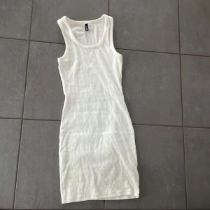 Vit ribbad kortklänning från H&M Divided - Säljer en vit ribbad kortklänning från H&M Divided. Klänningen är ärmlös med rund halsringning och har en tight passform. Perfekt för varma dagar och enkel att styla med olika accessoarer.