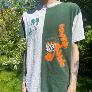 Grön och grå t-shirt med Mickey Mouse Disney tryck - Säljer en tvåfärgad t-shirt från Disney med Mickey Mouse-tryck och texten 'Slam Dunk' samt basketmotiv på framsidan. En klassiker!