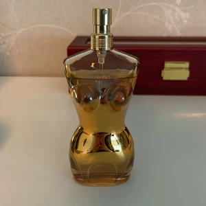 Jean Paul Gaultier Classique Eau de Parfum Intense - En ikonisk parfymflaska i form av en kvinnlig byst, tillverkad i genomskinligt glas med gyllene toner. Flaskan har en elegant och sensuell design med metallisk gulddetalj vid halsen och spraymunstycke. Rymmer 100 ml parfym. Är ca 90 ml kvar.