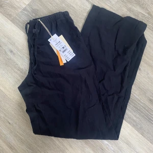 Svarta linnebyxor från Gina Tricot - Svarta linnebyxor från Gina Tricot med resår i midjan och rak passform. Byxorna är i modellen 'tall' och har en enkel, stilren design utan synliga detaljer. Perfekta för en avslappnad och trendig look.