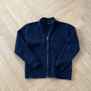 Mörkblå stickad kofta med dragkedja - Säljer en mörkblå stickad kofta med dragkedja framtill. Koftan har lång ärm och hög krage, perfekt för kyligare dagar. Enkel och stilren design som passar till det mesta. Storlek är 12A så passar dom som är 12år säljer den för jag har växt ur den, skriv vid minsta tanke