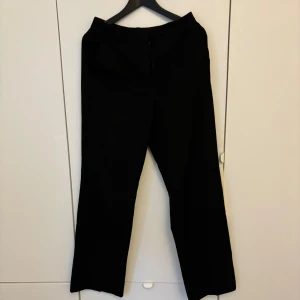 Svarta kostymbyxor från BikBok - Svarta kostymbyxor från BikBok med klassisk rak passform och normal midja. Byxorna har diskret dragkedja framtill och är perfekta för en stilren look. Materialet känns mjukt och följsamt.