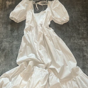 Vit långklänning med puffärmar och volang - Säljer en romantisk vit långklänning med puffiga kortärmar, fyrkantig ringning och knytband i ryggen. Klänningen har volangdetaljer och är tillverkad i ett lätt bomullstyg. Perfekt för sommarens alla tillfällen!