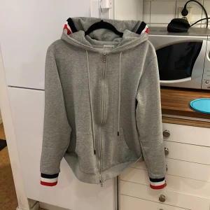  Moncler - Säljer en stilren grå hoodie från Moncler med dragkedja och randiga detaljer i rött, vitt och blått på ärmslut och huva. Perfekt för en avslappnad look. Riktigt snygg och inga fläckar eller liknande. Hör av er vid funderingar. Är storlek XXL men passar storlek L perfekt