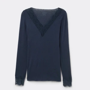 Mörkblå långärmad topp med spetsdetaljer - Säljer en mörkblå långärmad topp med v-ringning och fina spetsdetaljer vid halsringningen och ärmsluten. Toppens material är mjukt,ganska tunt och stretchigt, perfekt för en stilren look.