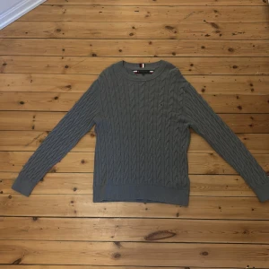 Grå kabelstickad tröja från Tommy Hilfiger - Säljer en klassisk grå kabelstickad tröja från Tommy Hilfiger med rund halsringning och diskret logga på bröstet. Perfekt för lager-på-lager och passar till det mesta. Mjuk och bekväm med ribbade muddar. Aldrig använd. Nypris runt 1800kr vårt pris 499kr! Priset kan förhandlas vid snabb affär.