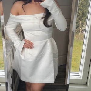 Vit offshoulder satin klänning från Odd Muse student/examen - Säljer denna otroliga vita offshoulder klänningen i satin från Odd Muse. Klänningen har lång ärm, markerad midja och kort kjol. Perfekt för dig som vill ha en elegant och stilren look. Modellen heter The Ultimate Muse Satin Bardot Mini Dress. Den är helt ny, prislapp kvar och passar perfekt till studenten/examen eller vilken annan tillsättning som helst!! Sitter superfint på, trendig och så smickrande😍 säljer pga att att jag hittat en annan klänning jag ska ha! Nypris 2 027kr🩷