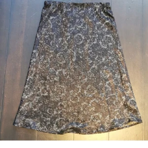 Svart mönstrad satinkjol - Säljer en svart satinkjol med subtilt mönster och lätt glansig yta. Kjolen har resår i midjan och är i en klassisk A-linjeform som slutar strax under knät. Perfekt för dig som gillar en stilren men ändå unik look.