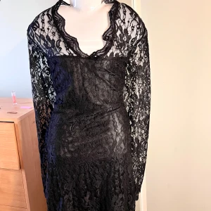 Svart spetsklänning med lång ärm - Säljer en svart klänning i spets med lång ärm och v-ringad hals. Klänningen har figurnära passform och vackra spetsdetaljer över hela plagget. Perfekt för dig som vill ha en elegant och stilren look.