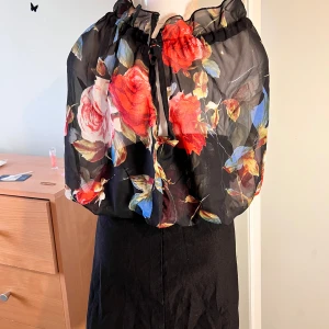 Blommig ärmlös klänning - Säljer en elegant ärmlös klänning med blommigt mönster i rött, blått och grönt på en svart bakgrund. Klänningen har en tight passform nertill och en luftigare topp. Perfekt för en somrig look!      Klänning stl M men lite som stl S