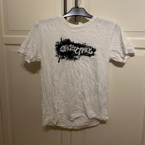 Vit t-shirt med svart graffiti-tryck - Vit  graphic t-shirt med ett stort svart graffiti-inspirerat tryck på bröstet. Klassisk rund hals och korta ärmar. Perfekt för dig som gillar streetwear och vill ha en enkel men cool look. I strl M