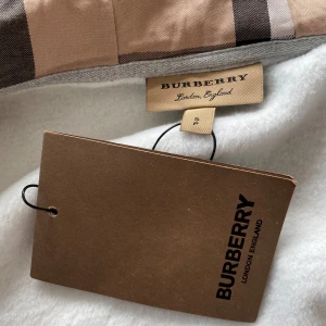Burberry hoodie - Säljer en snygg hoodie från Burberry med klassiskt beige rutigt mönster på insidan av huvan och vita partier på utsidan. inte ens använd och den har fortfarande taggen pris ej hugget i sten!!