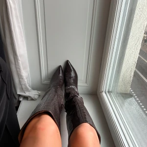 Bruna boots med klack - NAKD  - Säljer ett par bruna höga boots med spetsig tå och croco-mönstrad yta. Skorna har en klassisk bootsform och når upp till knäna. Med 7 cm klack och använda enstaka gånger💕💞ny pris 899