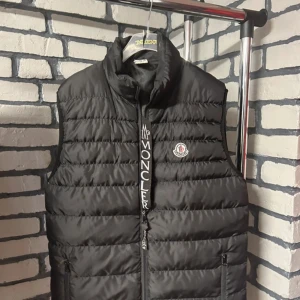 Svart dunväst från Moncler - pris är diskuterbart!  säljer en riktig fet moncler väst inför sommarn! den är i jätte bra skick förutom att det finns ett litet hål vid fickorna, men det är inte jätte synligt plus det går att fixa om du kan sy ihop det👍