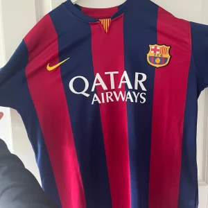 FC Barcelona Neymar Jr 11 matchtröja - Säljer en klassisk FC Barcelona fotbollströja med Neymar Jr och nummer 11 på ryggen. Tröjan är randig i rött och blått med gula detaljer, Qatar Airways som sponsor och klubbmärke på bröstet. Perfekt för fans av Barça!