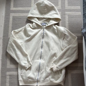 Beige ziphoodie  - Säljer en vit hoodie från Bolongaro Trevor i storlek M. Har små gul fläckar vid armen, men det går nog att ta bort i tvätten