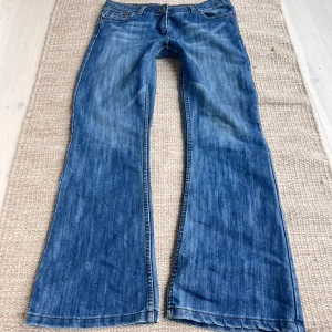 Blå bootcut jeans - Säljer ett par klassiska blå bootcut jeans med låg midja. Jeansen har fem fickor och stängs med dragkedja och knapp. Perfekta för dig som gillar en retroinspirerad look med utsvängda ben.